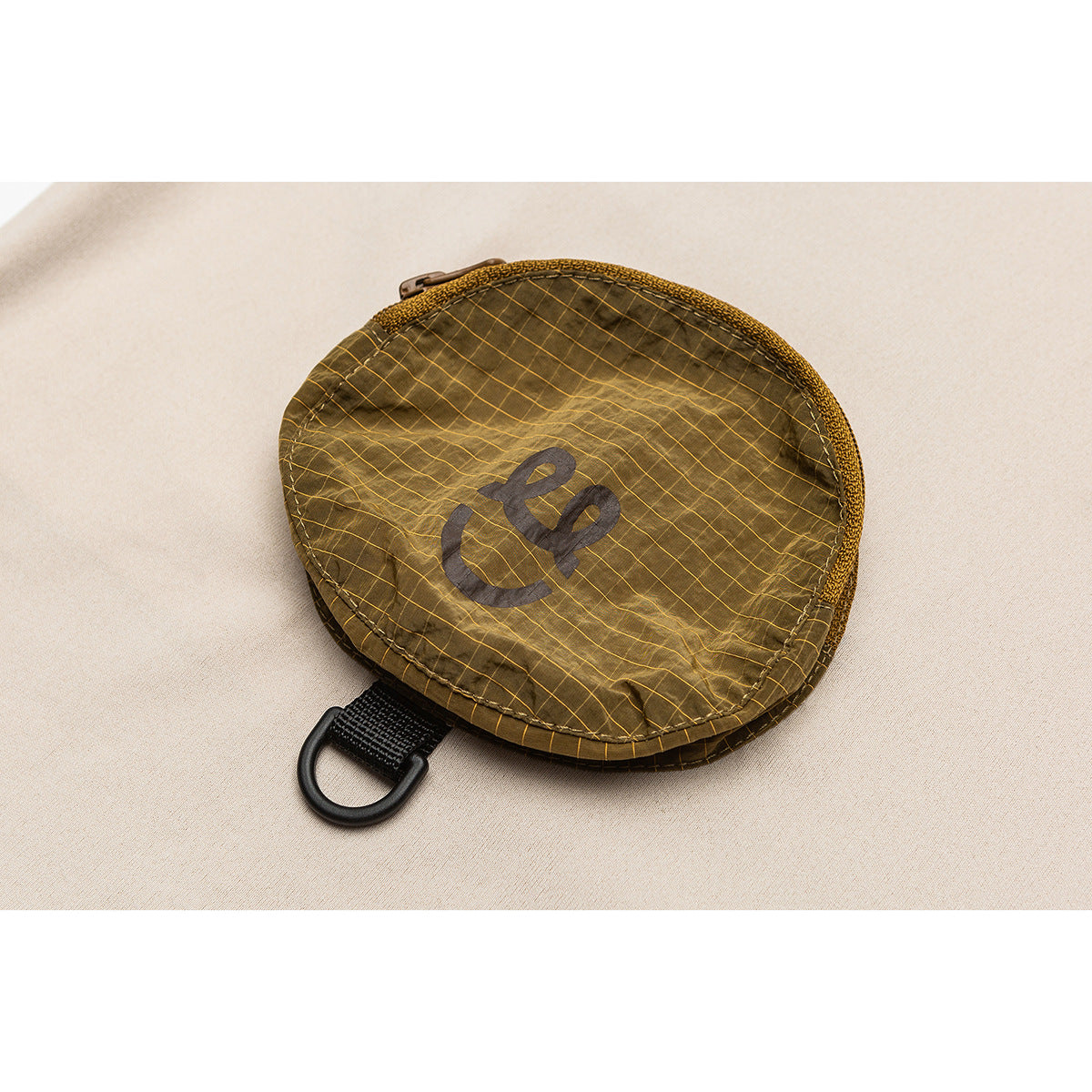 Close-up of a brown oval zip pouch with a yellow grid pattern and a black loop on beige fabric.