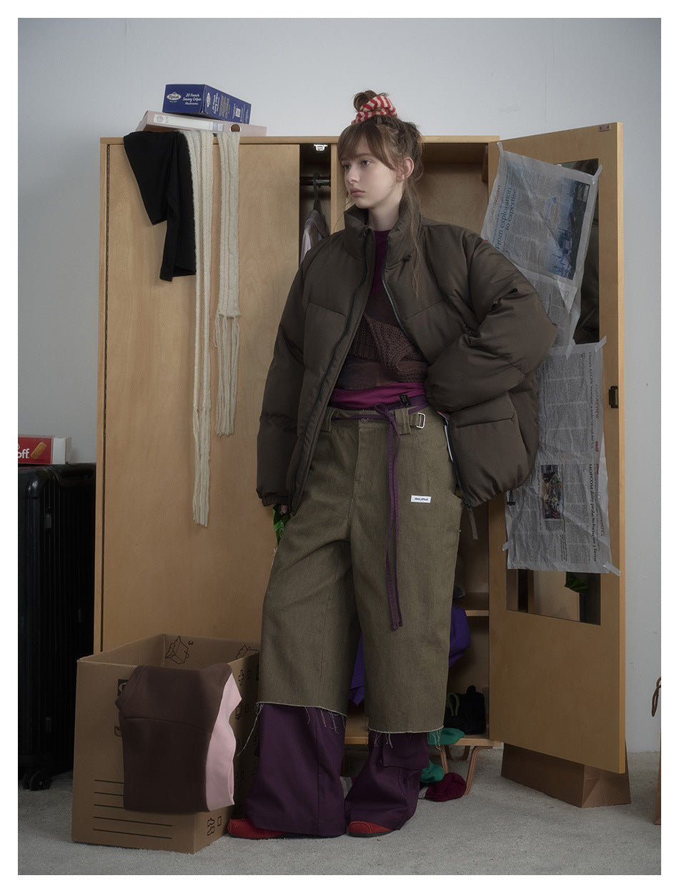 Model in an olive-green puffer jacket seen from the side with a hand in the pocket, styled with olive pants and purple layers