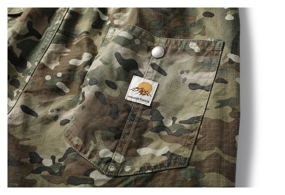 Close-up of a camouflage trouser pocket with a metal snap and a small mountain-logo fabric patch.