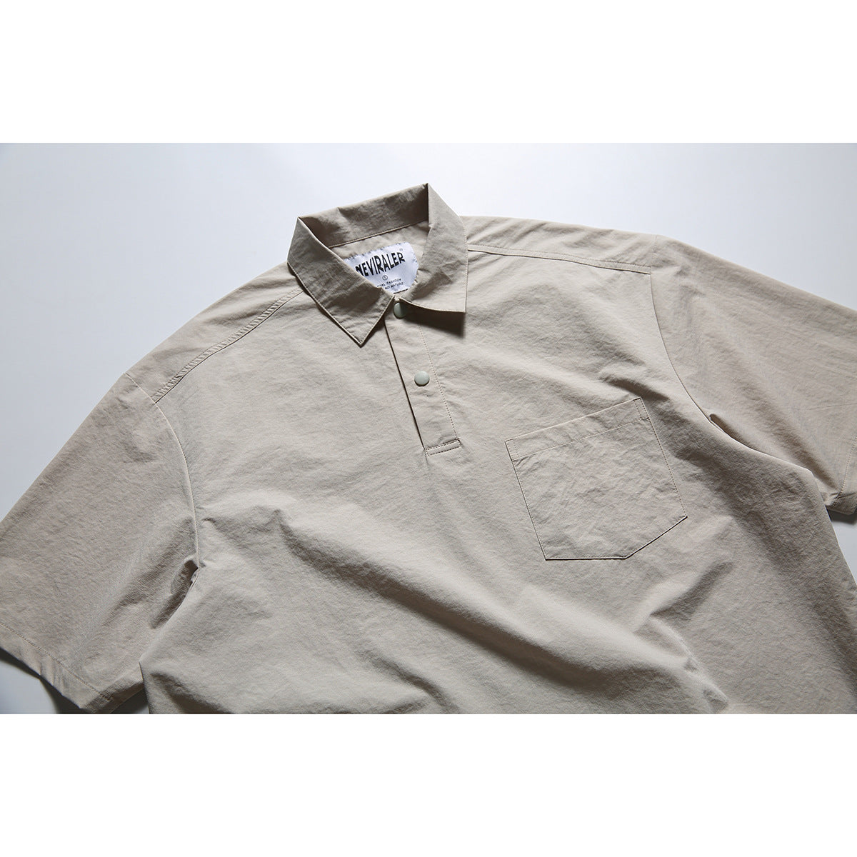 Close view of a light taupe short-sleeve polo shirt with a pointed collar, snap placket and chest pocket.