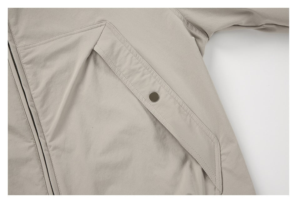 Close-up of an angled pocket flap with a dark snap button on the light taupe jacket.