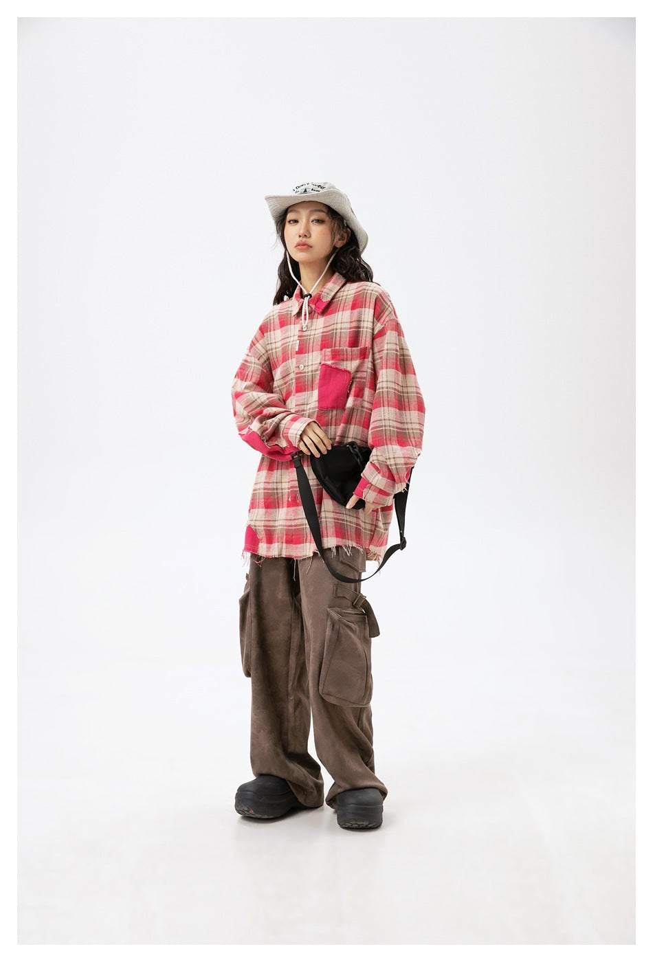 Full-length view of a model wearing a red plaid shirt with pink accents and loose brown cargo trousers.