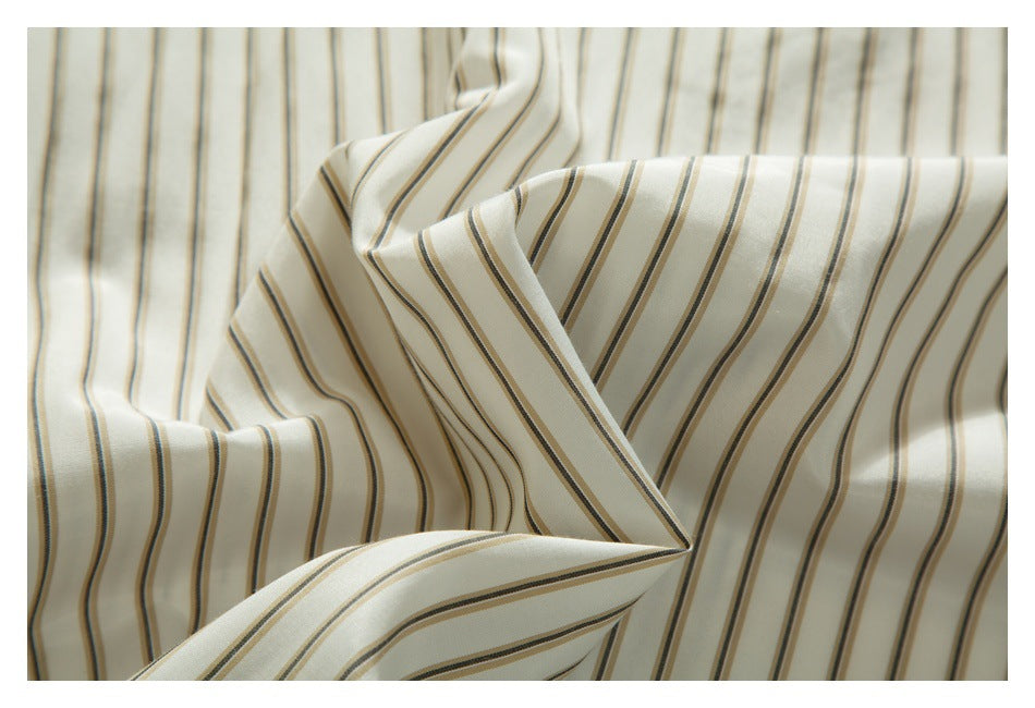 Close-up of draped ivory shirt fabric with narrow tan and dark gray stripes.