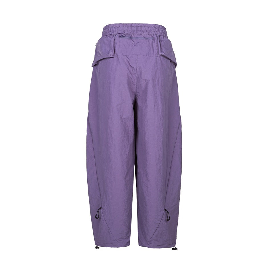 Back view of purple wide-leg pants with elastic waistband, back yoke zip pocket, flap pockets and drawcord hems