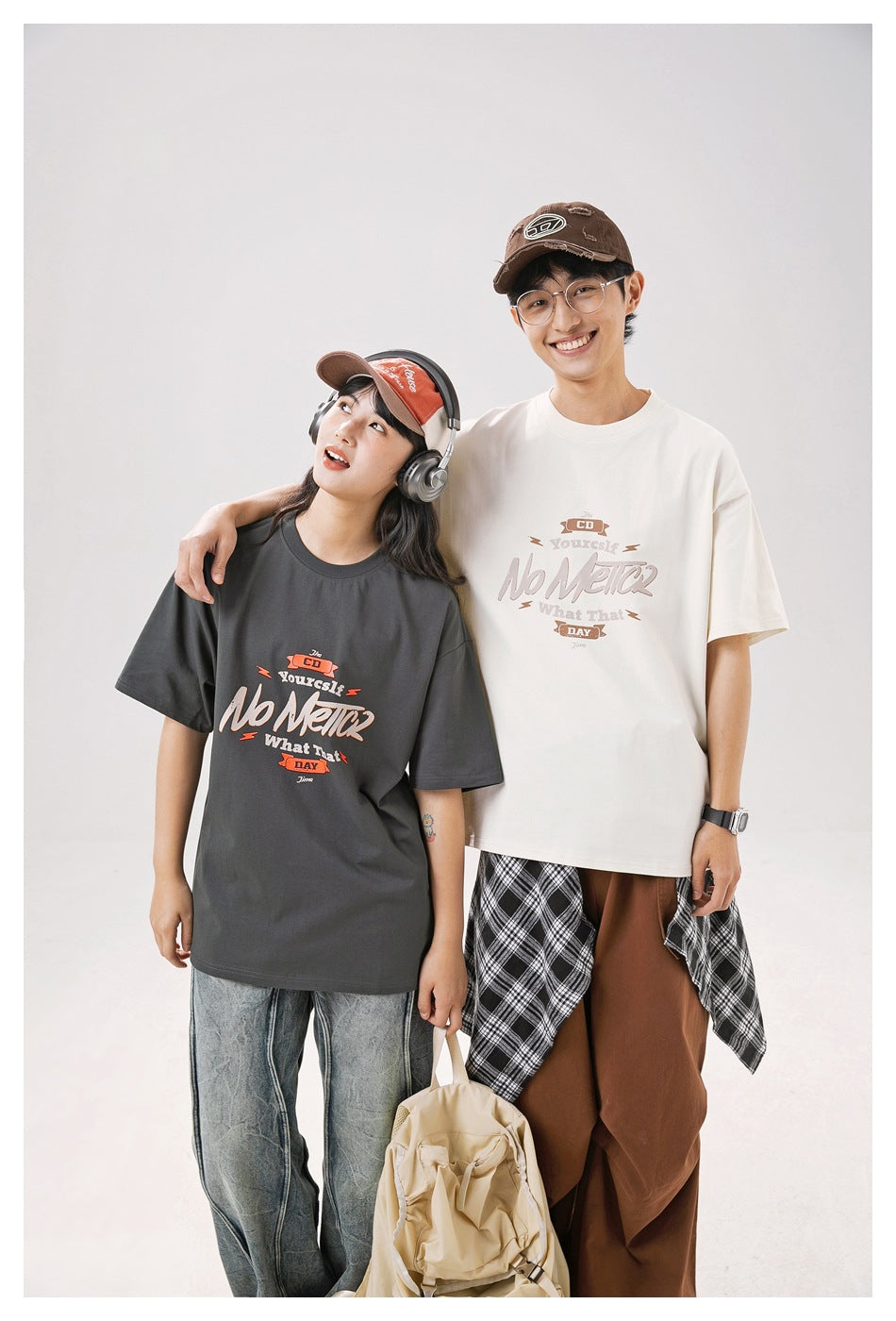 Two models stand together wearing charcoal and off-white oversized graphic T-shirts.