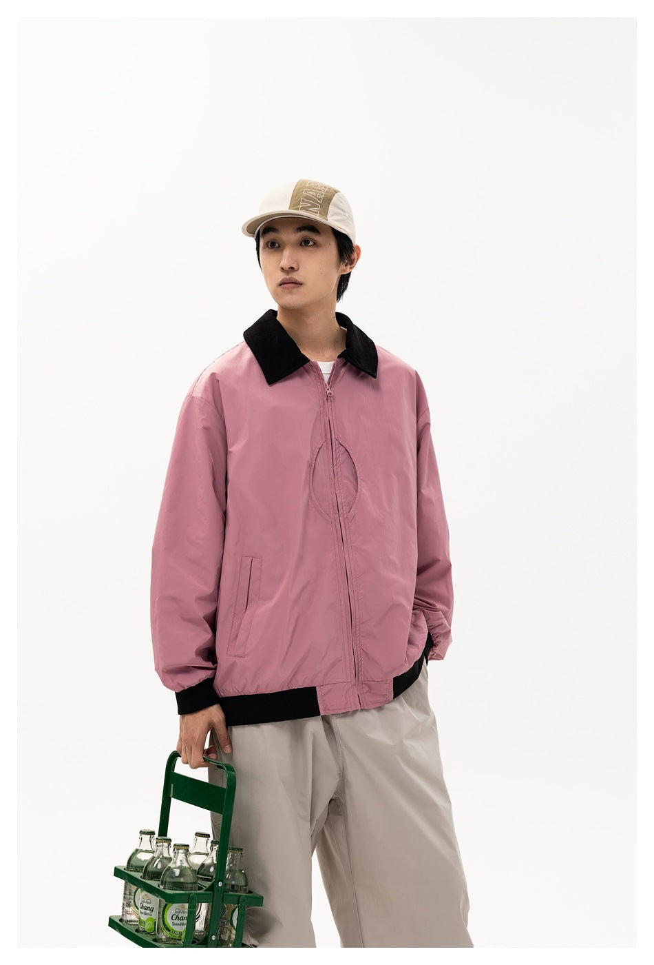 Model wearing a pink zip-front jacket with a black collar and trim, beige cap, and light trousers.