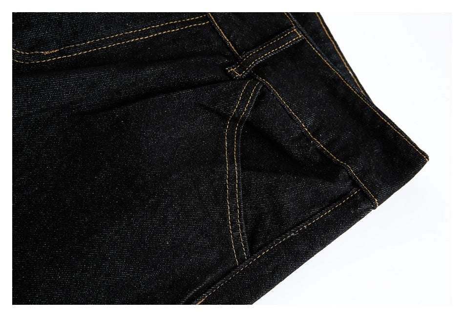 Close-up of a curved front pocket and gold-stitched seams on black jeans.