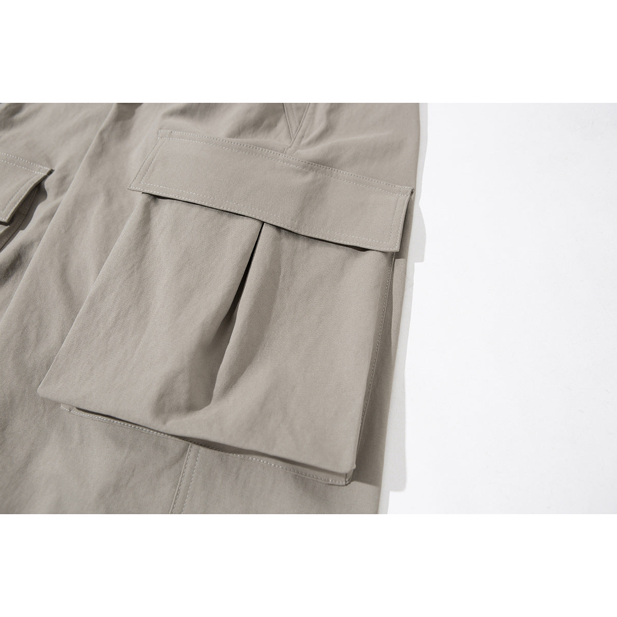 Close-up of a taupe cargo pants leg with a large flap pocket and visible stitching.
