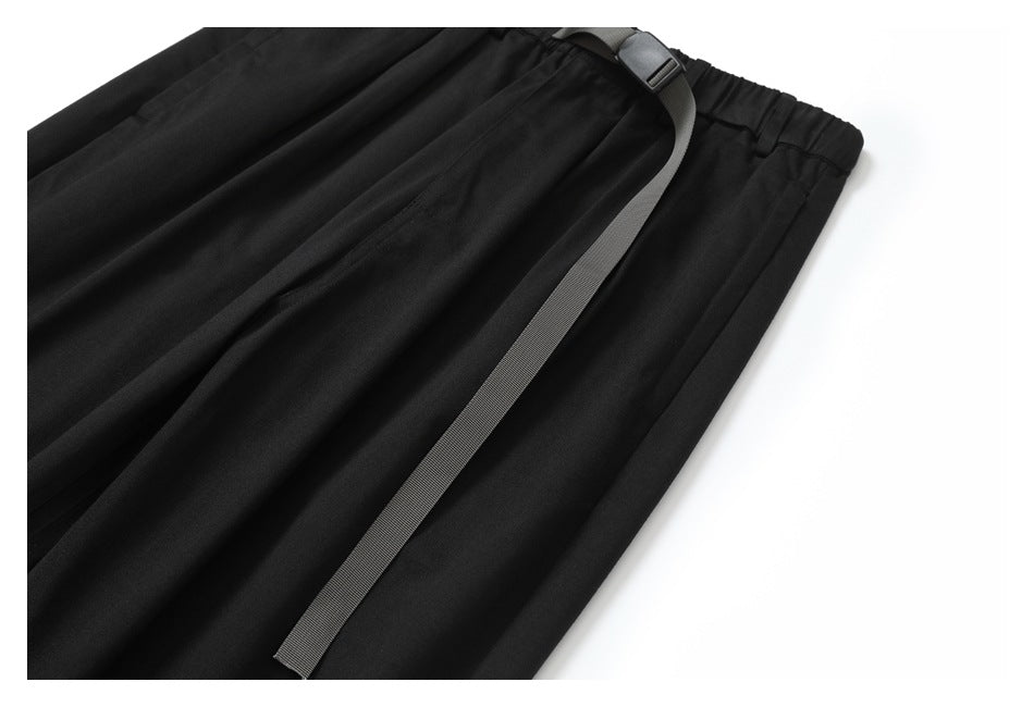 Close view of black trousers and their long gray webbing belt, showing the waistband and front pleats.
