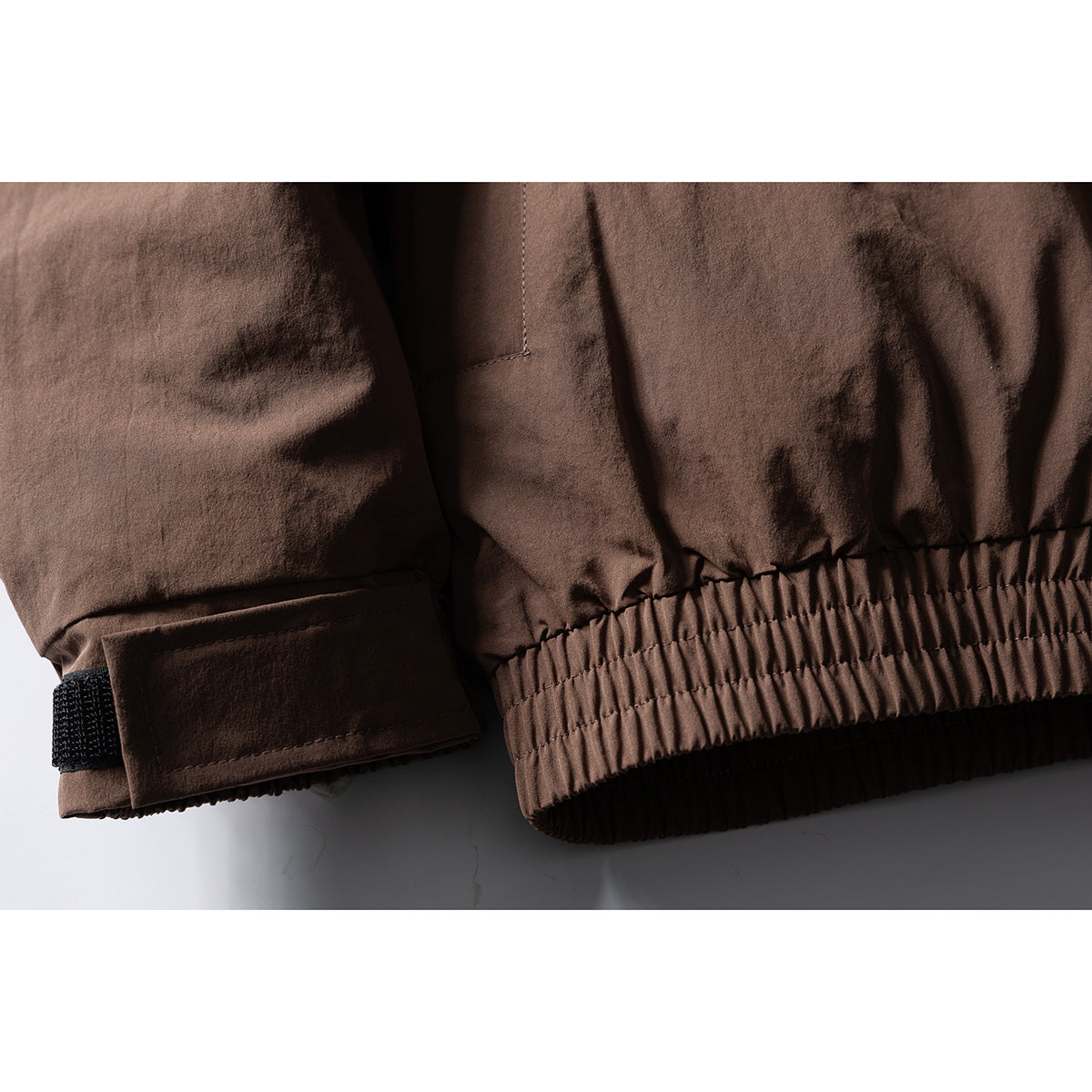 Close-up of a brown jacket's elastic hem and adjustable sleeve cuff with a black tab.