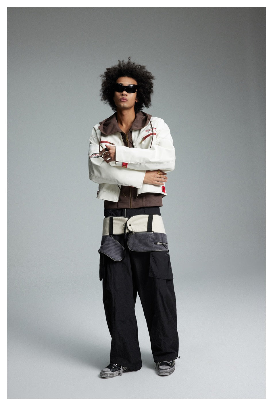 Model wearing a cream jacket with brown hood and red details, layered over a brown zip top with black cargo trousers.