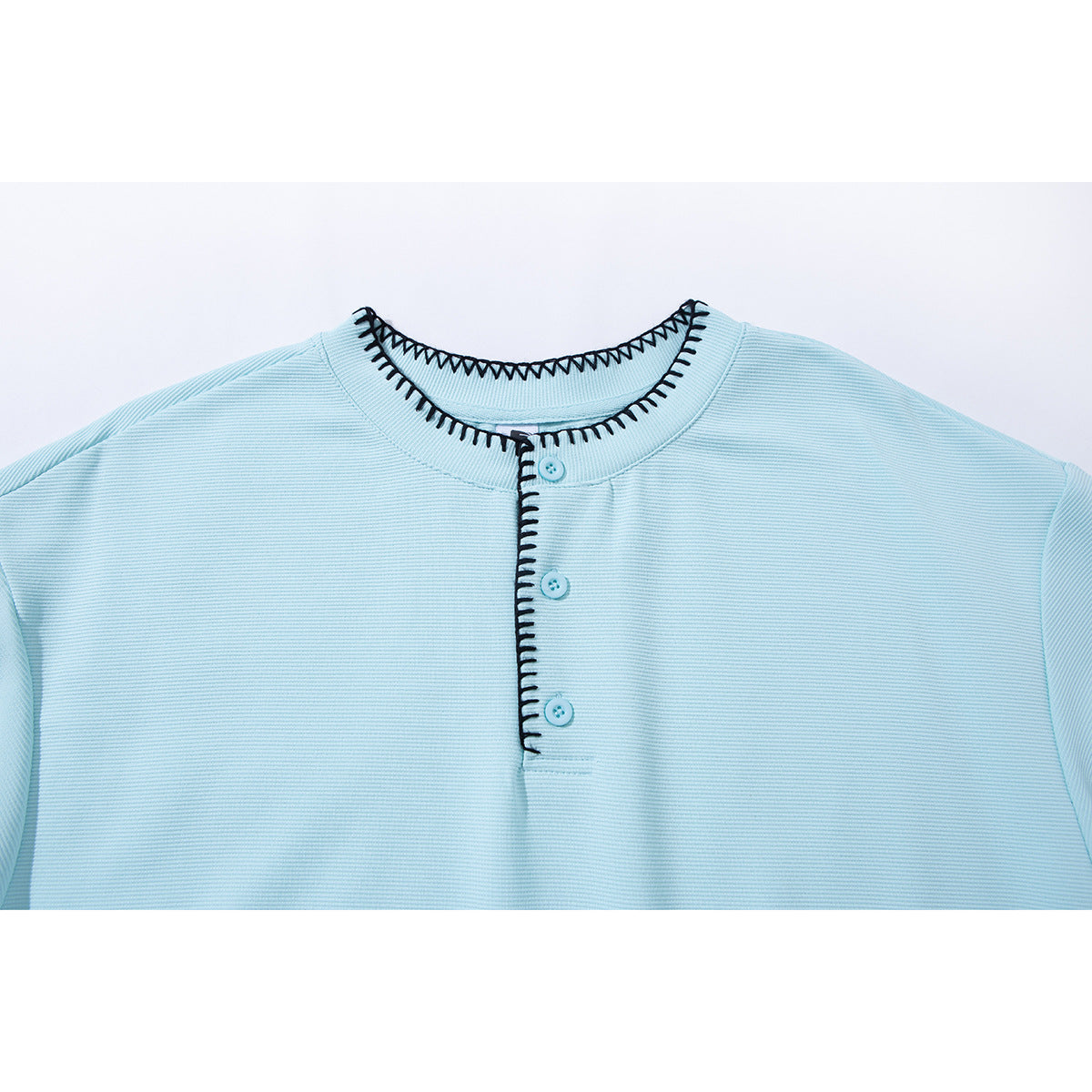 Close-up of a pale blue shirt neckline and three-button placket with black contrast stitching.
