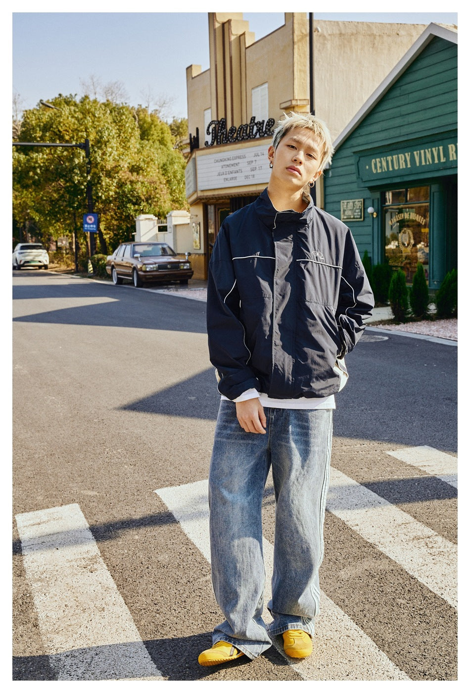 Full-length view of a model wearing a navy jacket with white piping and loose blue jeans.
