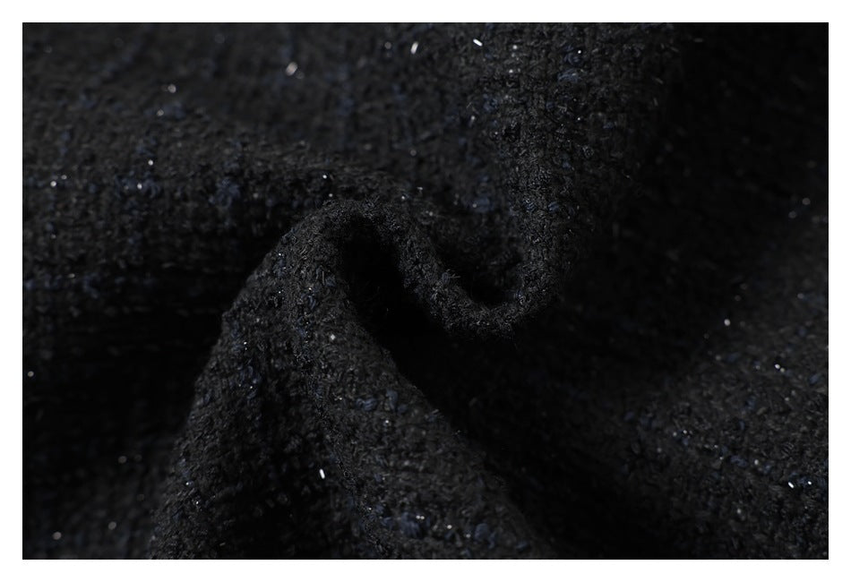 Close-up of black textured fabric gathered into a soft fold, with scattered light flecks.