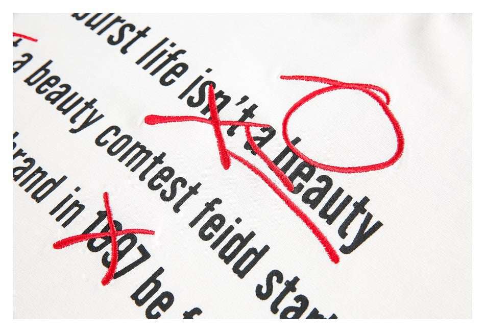 Tight close-up of black English lettering crossed by red embroidery on white fabric.