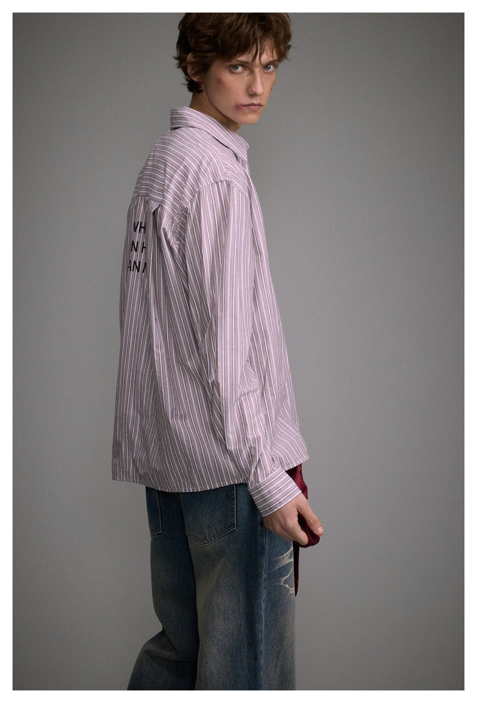 Side view of a model wearing a loose pink-and-white striped shirt with partial black lettering on the sleeve.