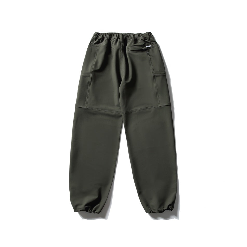 Back view of dark olive utility pants with an elastic waist, rear zip pocket, stitched panels, and gathered cuffs.