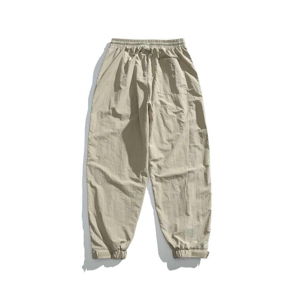 Back view of light beige jogger pants laid flat, with an elastic waist, tapered legs, elastic cuffs and a rear pocket.