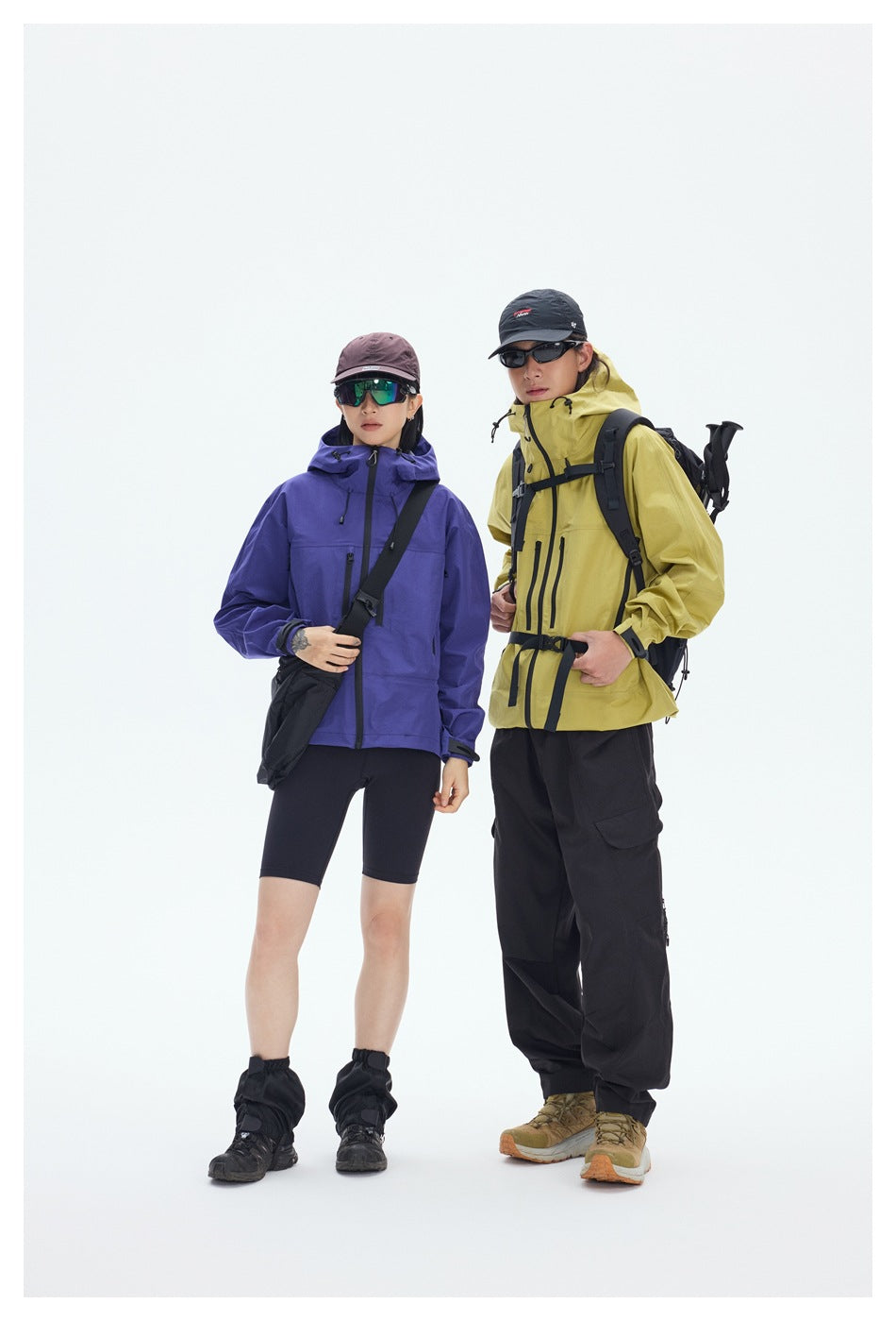 Two hikers model outdoor clothing: a purple jacket and black shorts, and a yellow jacket with black pants.