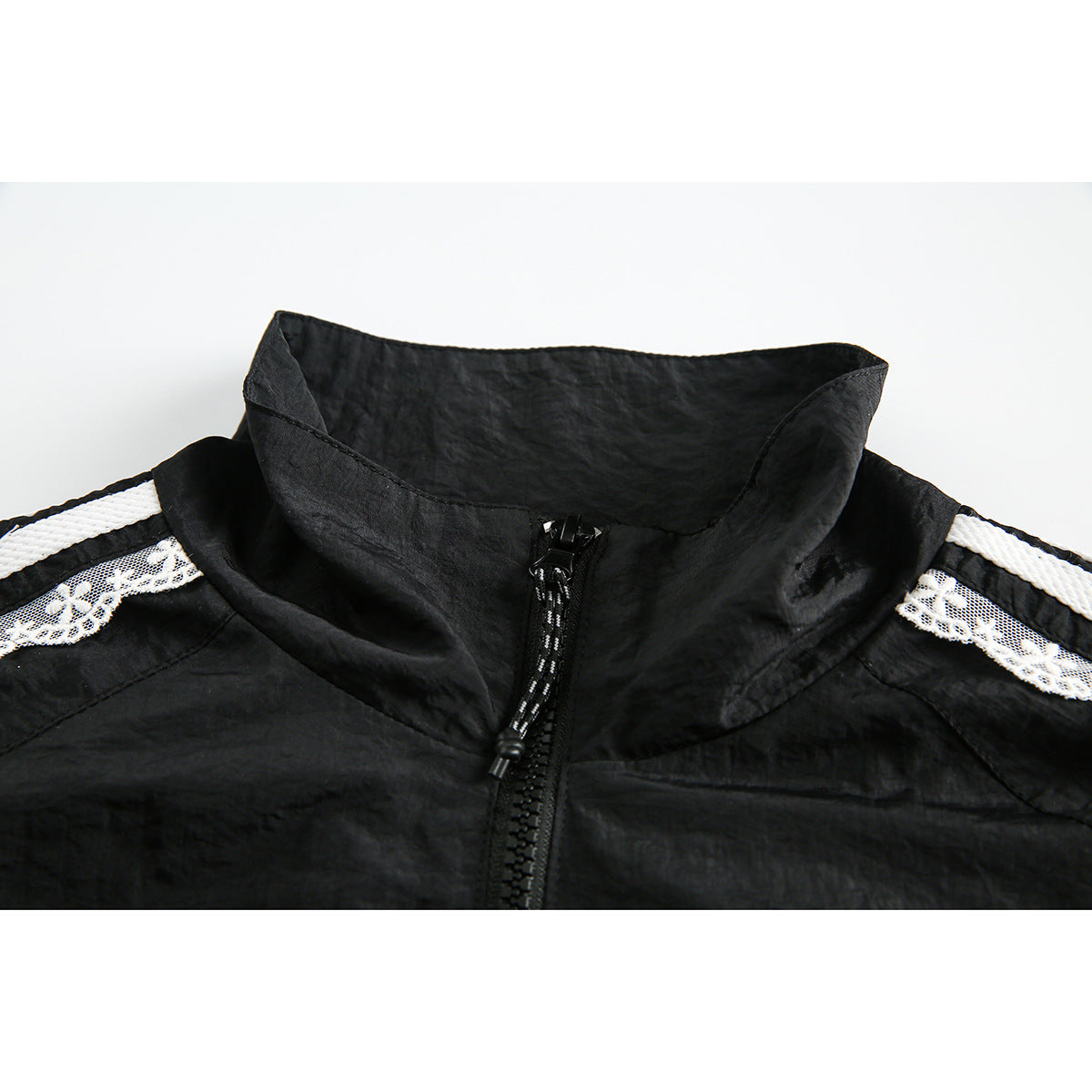 Close-up of a black jacket's tall collar and front zipper, with white lace and stripe trim across the shoulders.