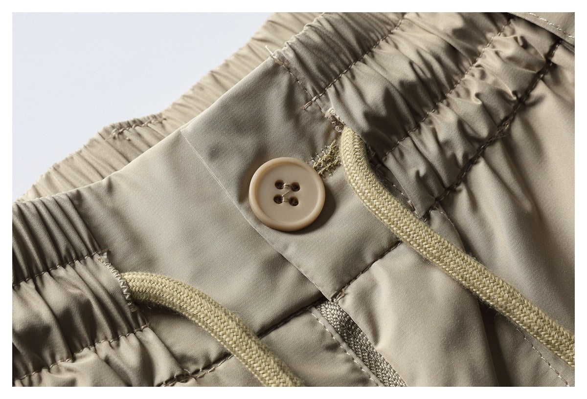 Detailed view of beige trousers with a four-hole button, elastic waistband, and braided drawstring.