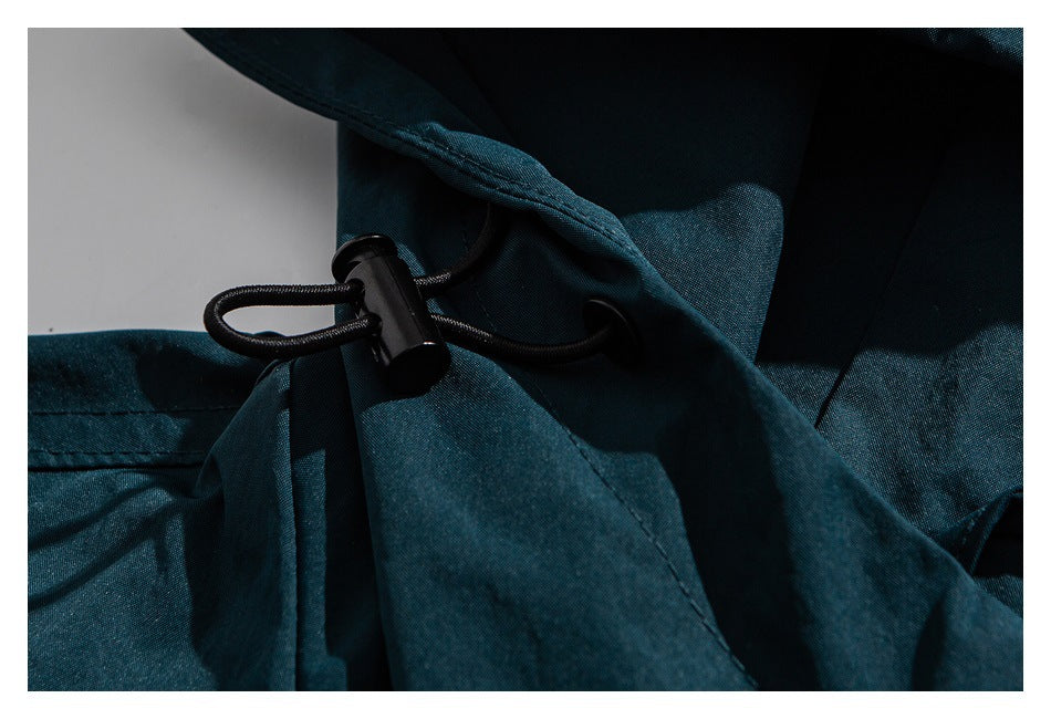 Close-up of a black cord lock and drawcord on dark teal garment fabric.