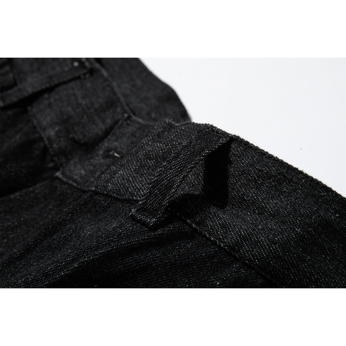Close-up of a black denim belt loop and reinforced stitching.