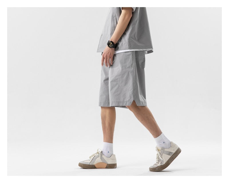 Side view of a person wearing gray relaxed knee-length shorts with notched side hem, matching top and sneakers