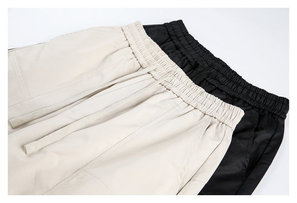 Close-up of beige and black pants showing gathered elastic waistbands, drawstrings, and stitched panels.