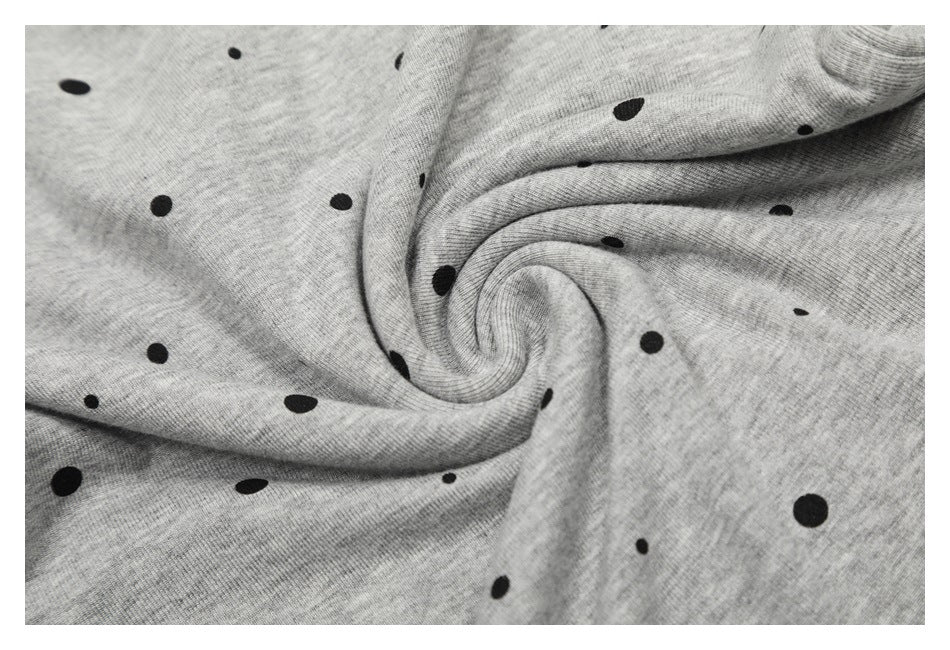 Close-up of gray fabric with scattered black polka dots, arranged in soft folds.