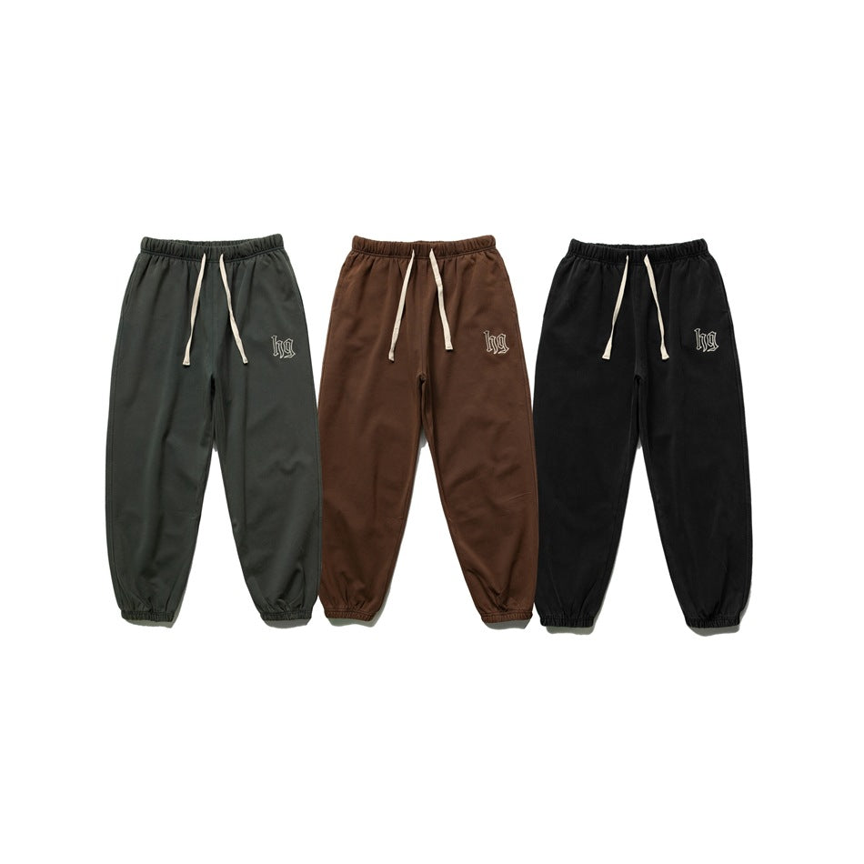 Front view of joggers in dark green, brown, and black, with cream drawstrings and small embroidered motifs.