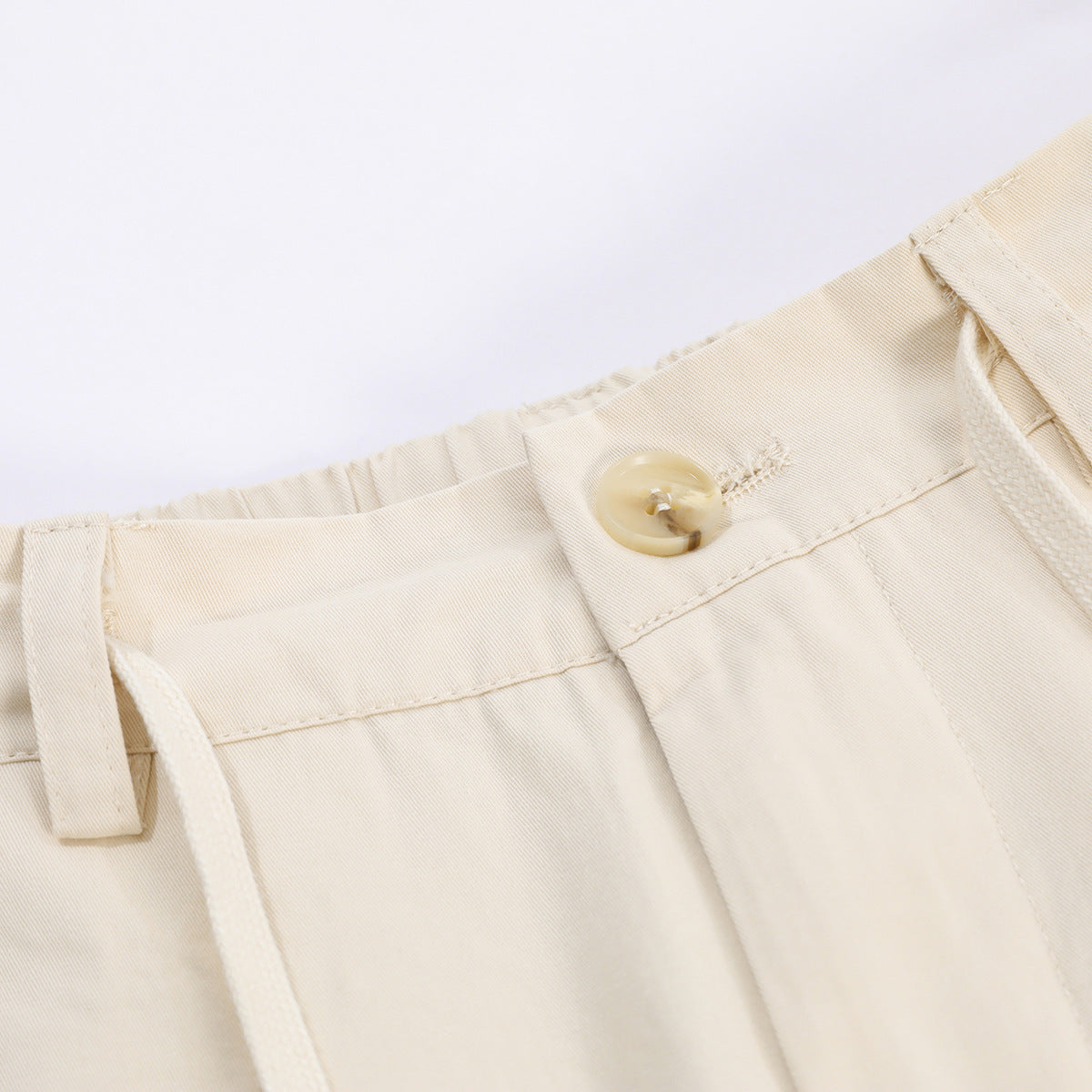 Close-up of cream trousers showing the waistband, button, belt loop, and drawstring.