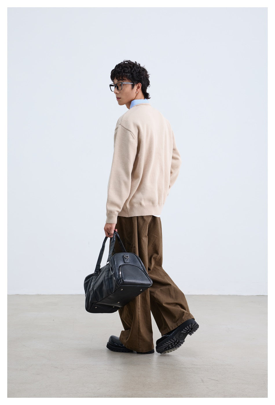 Rear three-quarter view of a model wearing a beige sweater and brown trousers.