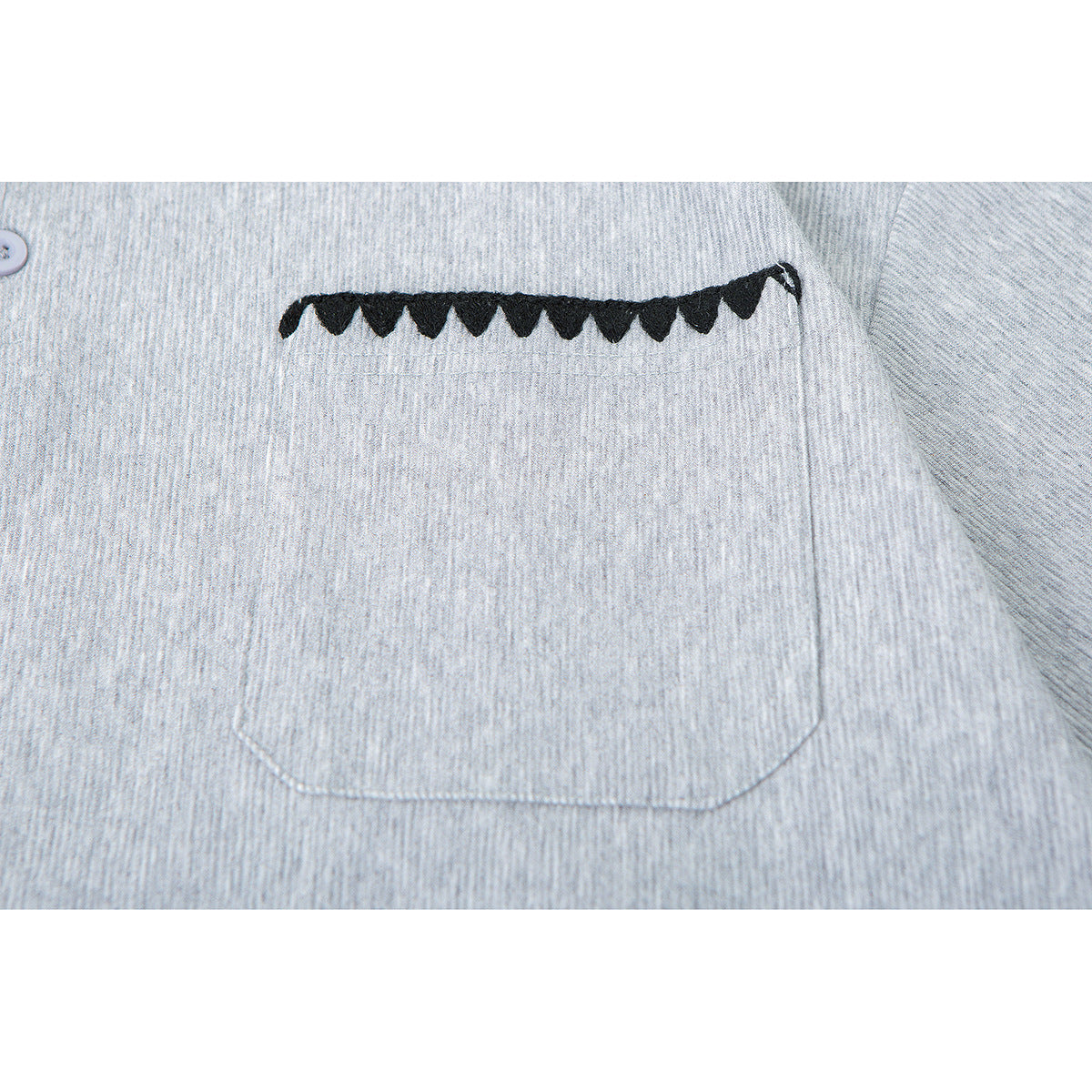 Close-up of a light gray polo shirt’s chest pocket with black scalloped trim.