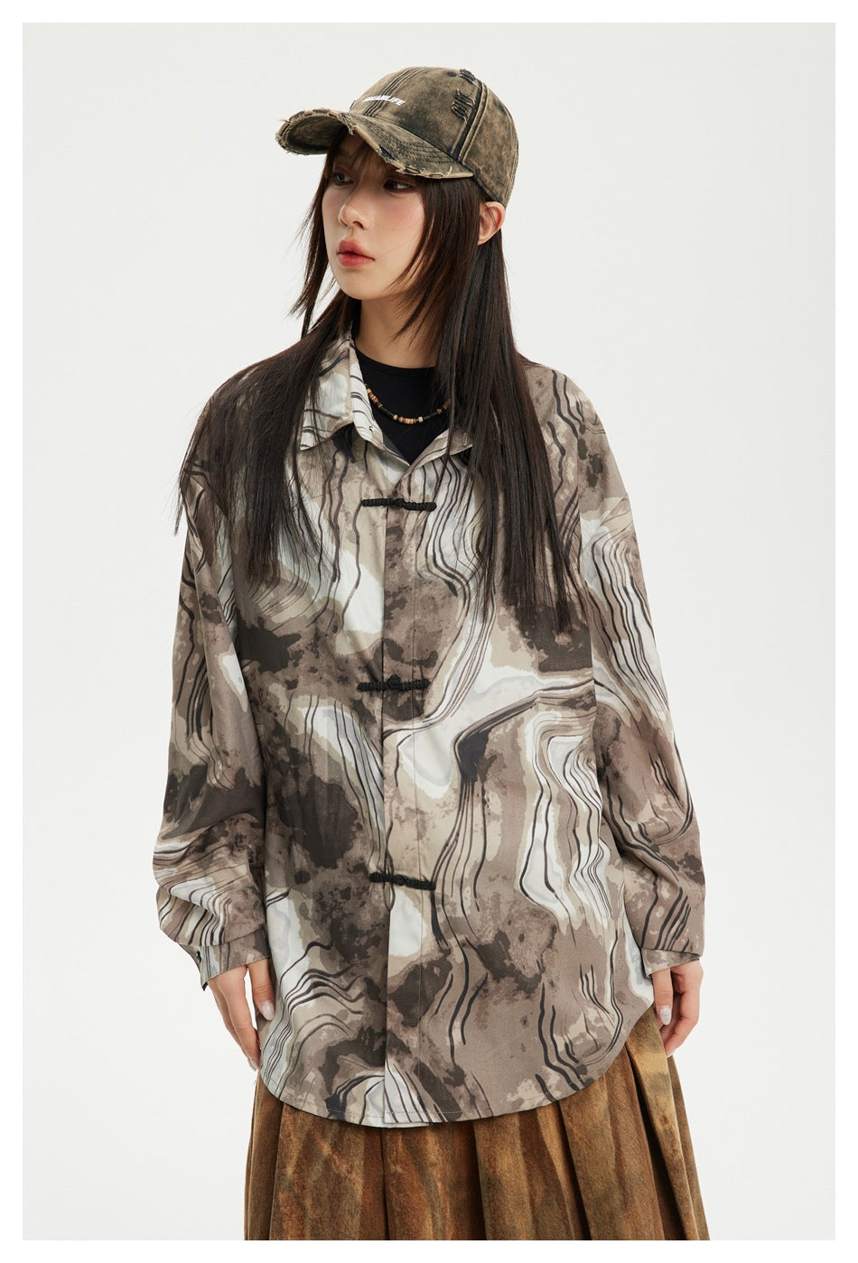 Model wearing a loose brown, taupe, and ivory abstract-print shirt with black frog closures, shown from the front.