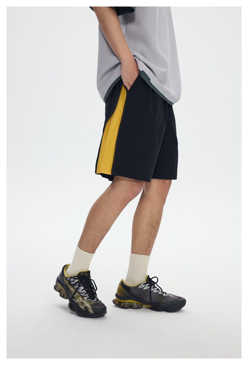 Side view of a model wearing black shorts with a mustard-yellow side panel and a light gray shirt.