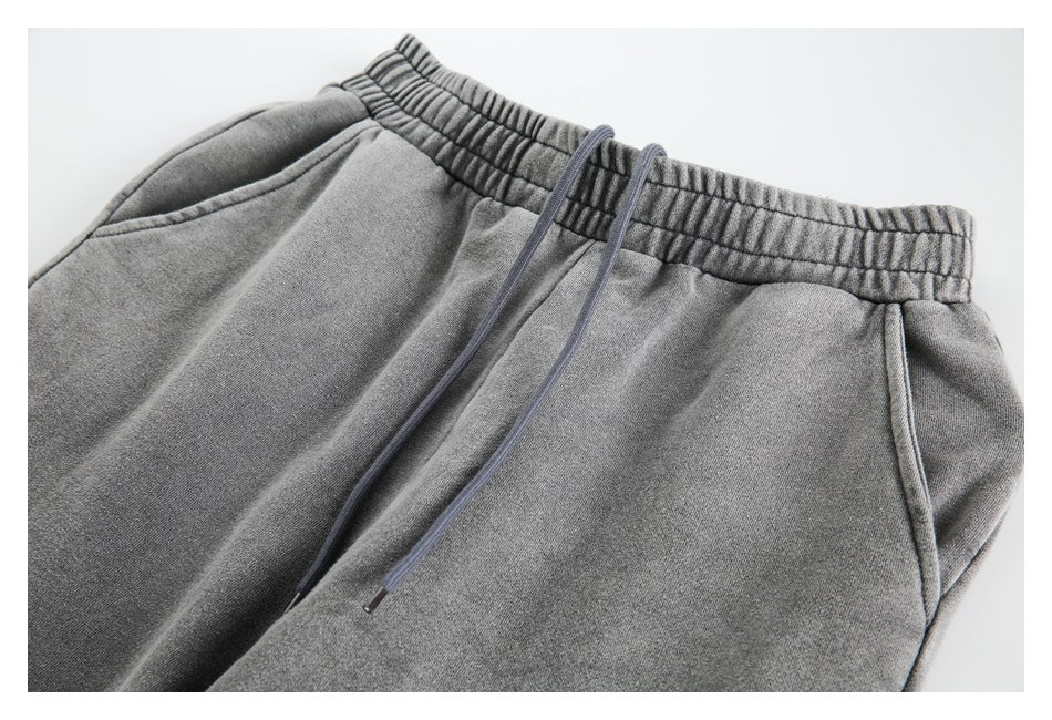 Close-up of gray sweatpants showing the gathered elastic waistband, drawstrings, and side pockets.