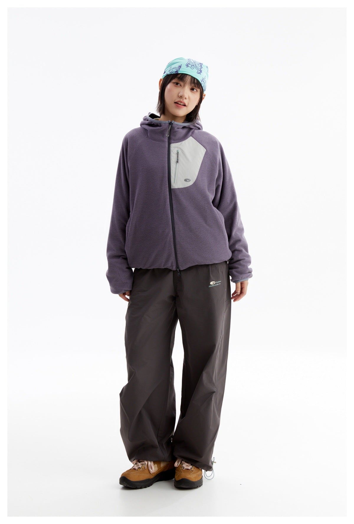 Full-length model wearing a purple hooded zip jacket with a pale chest pocket, dark wide-leg pants and hiking shoes.