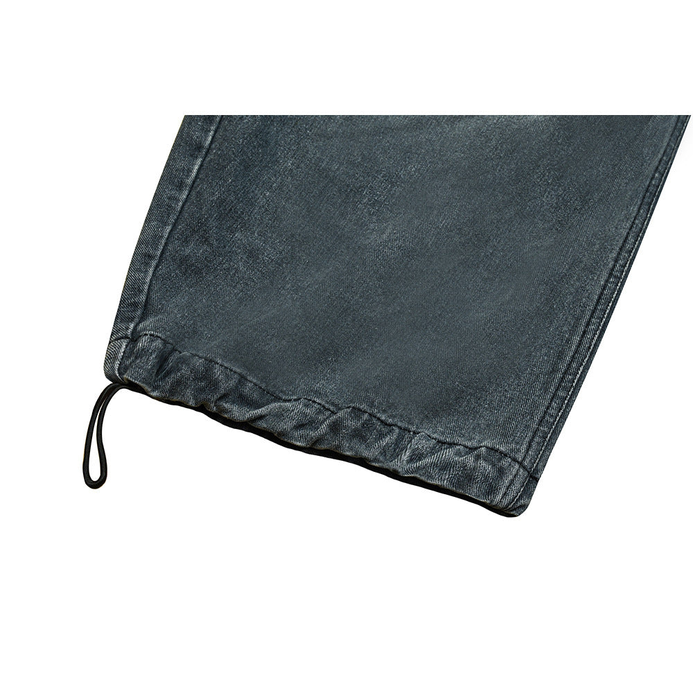 Close-up of a dark gray denim pant leg hem with a black drawcord loop.