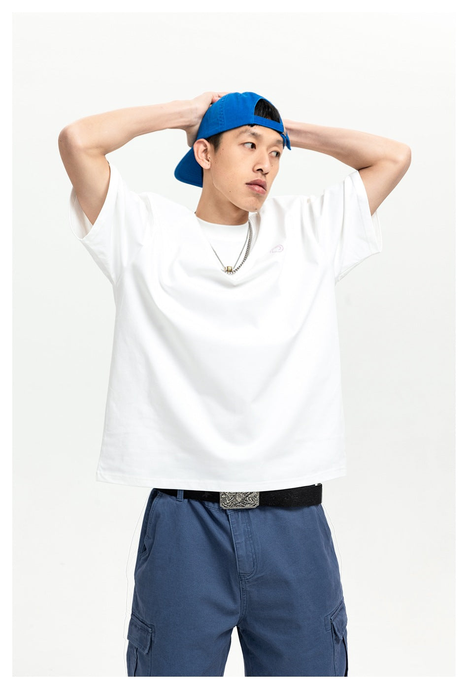 Front view of a man in a white oversized T-shirt with a small chest emblem and blue cargo pants.