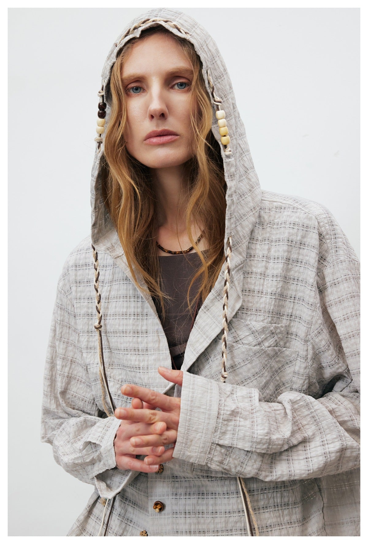 Close-up of a model wearing a light gray plaid hooded jacket with braided, beaded drawstrings.