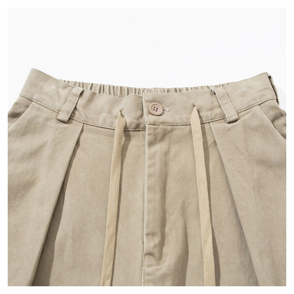 Close-up of beige trousers showing the buttoned waistband, belt loops, pleats and long drawstrings.