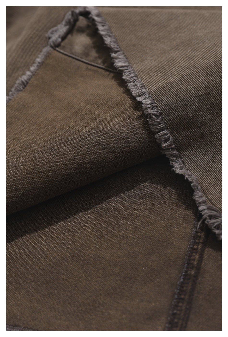 Close-up of brown-gray garment fabric folded to show its frayed edge and stitching.