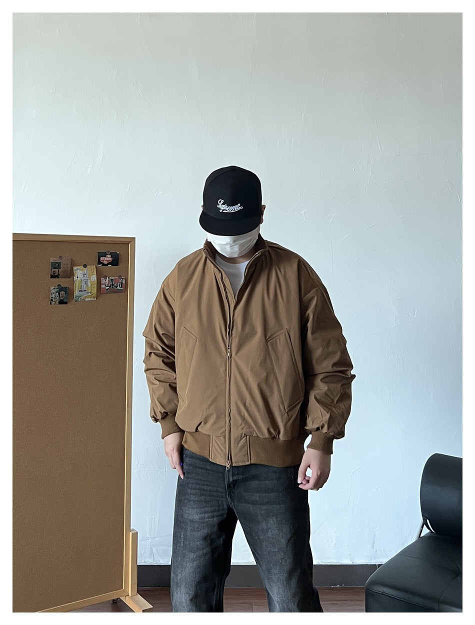 Person wearing the brown zip-up puffer jacket with slanted pockets and ribbed cuffs, with dark jeans and black cap