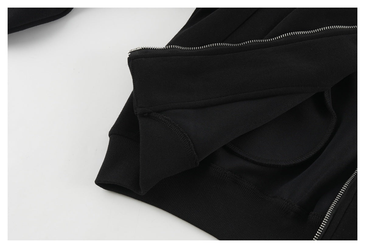 Close-up of a black garment showing a silver zipper, curved pocket opening, and ribbed cuff.