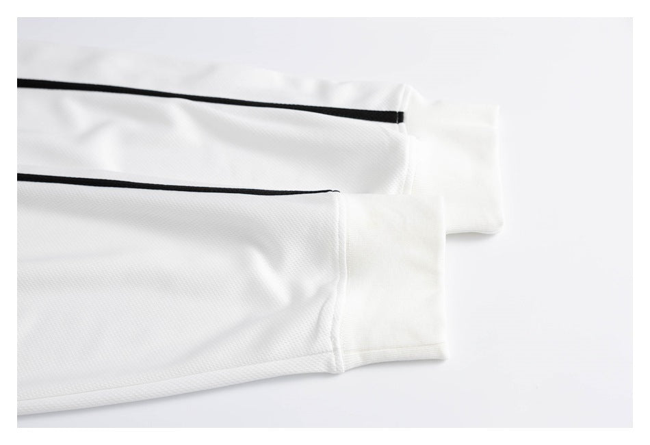 Close-up of white jersey sleeve cuffs with narrow black piping and stitched hems.
