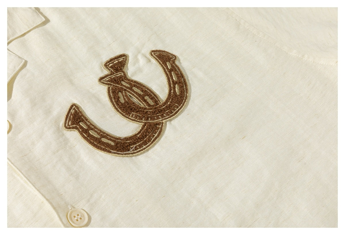 Close-up of brown horseshoe embroidery on a cream shirt beside its button placket.