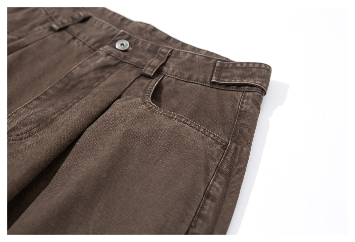 Close-up of the brown trousers' front waistband, button, belt loop, and curved pocket opening.