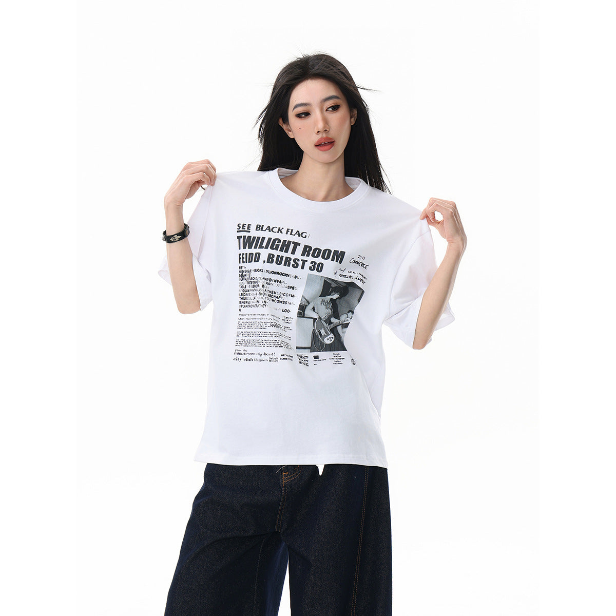 Model holds out a white oversized T-shirt with a black concert-poster-style graphic across the front.