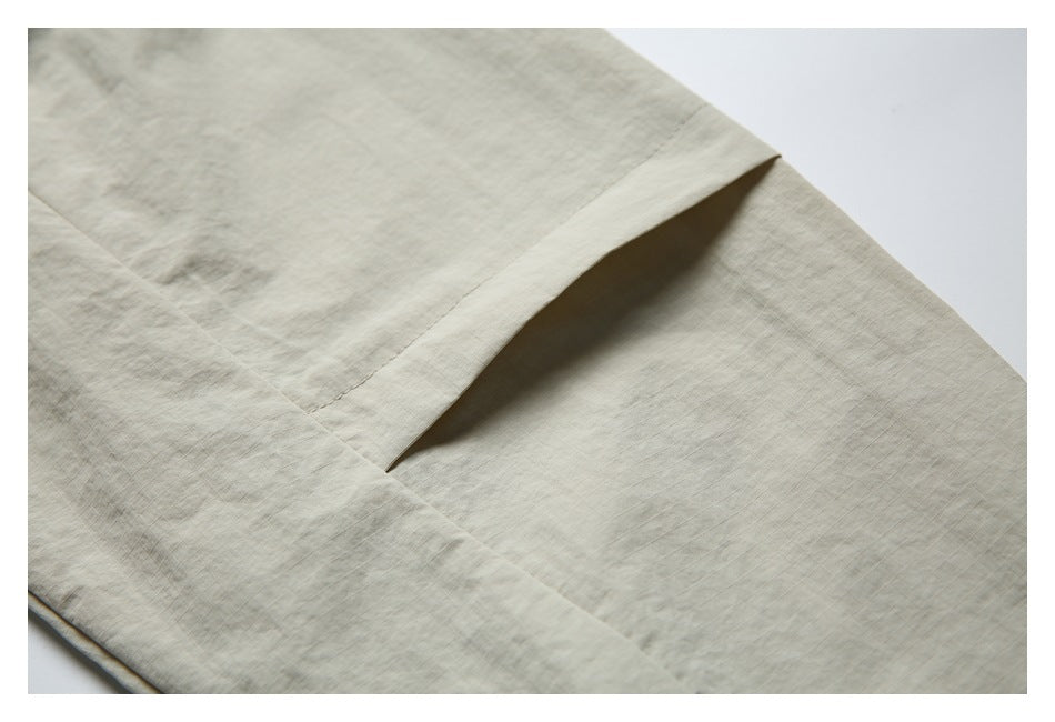 Close-up of a horizontal folded pleat and stitching on the light beige shirt.